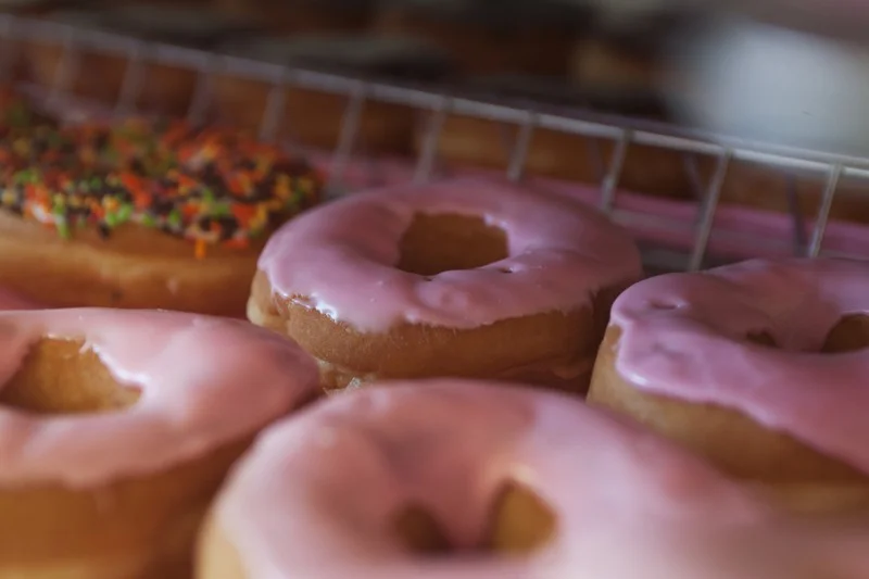 several donuts topped with pink glaze on a tray